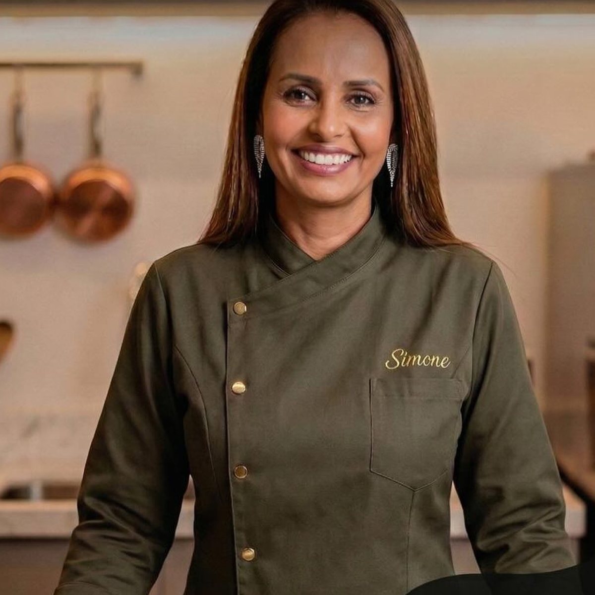 Simone Oliveira sorrindo, de dólmã verde, na cozinha